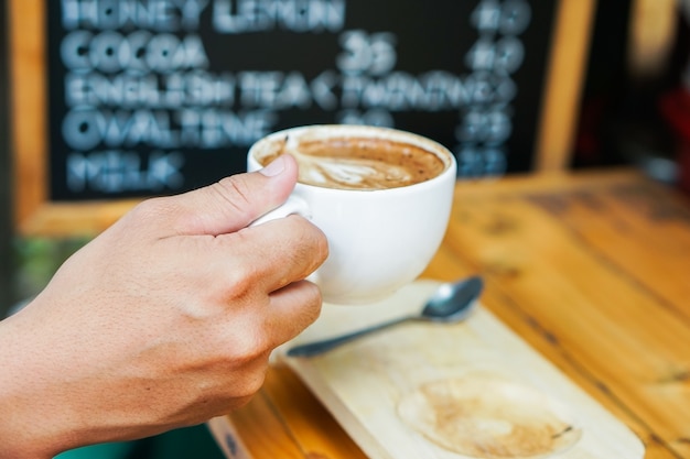 Equipaggi la mano che tiene una tazza da caffè di Latte Art.