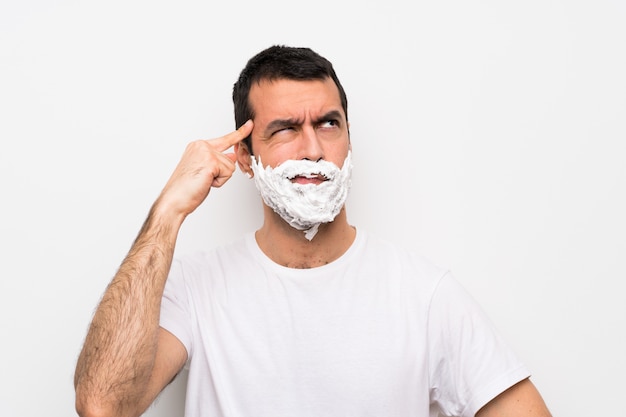 Equipaggi la rasatura della sua barba sopra bianco isolato che ha dubbi e pensiero