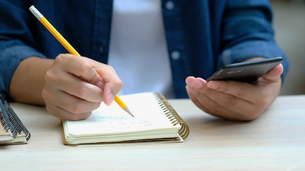 Equipaggi la scrittura sul taccuino mentre per mezzo del telefono cellulare