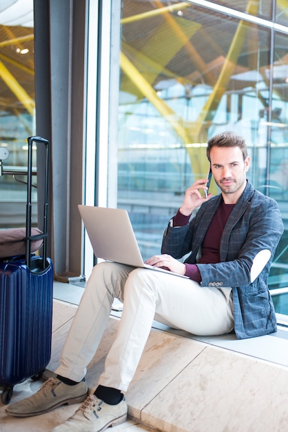 Equipaggi la seduta all'aeroporto facendo uso del computer portatile e del telefono cellulare accanto alla finestra