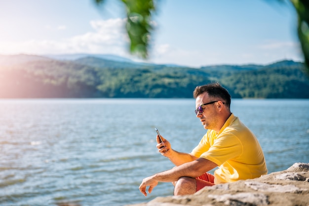 Equipaggi la seduta su una spiaggia e per mezzo dello Smart Phone