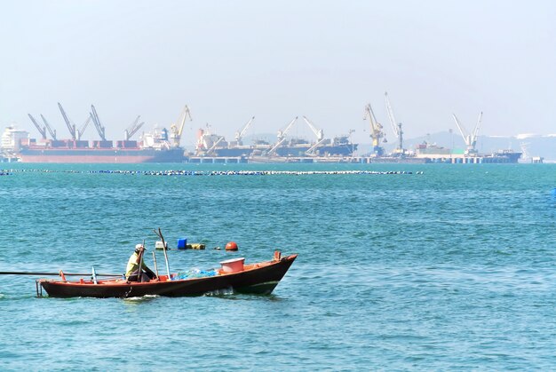 Equipaggi la seduta sulla piccola barca di legno nel mare che esamina il porto del mare sui precedenti