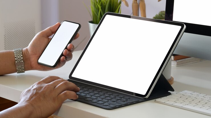 Foto equipaggi la tenuta del telefono cellulare dello schermo in bianco mentre lavorano con la tastiera astuta del ridurre in pani