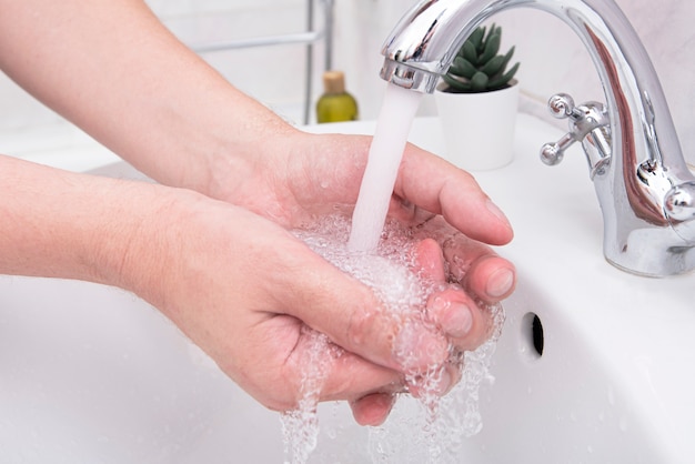 Equipaggi lavare le sue mani, mani del primo piano dell'uomo al bagno con sapone e flusso dell'acqua, immagine di concetto sull'igiene