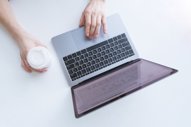 Equipaggi lavorare ad un computer portatile e la tenuta della tazza di caffè su una priorità bassa bianca