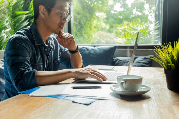 Equipaggi lavorare al computer portatile con la carta del documento e la tazza di caffè sullo scrittorio di legno