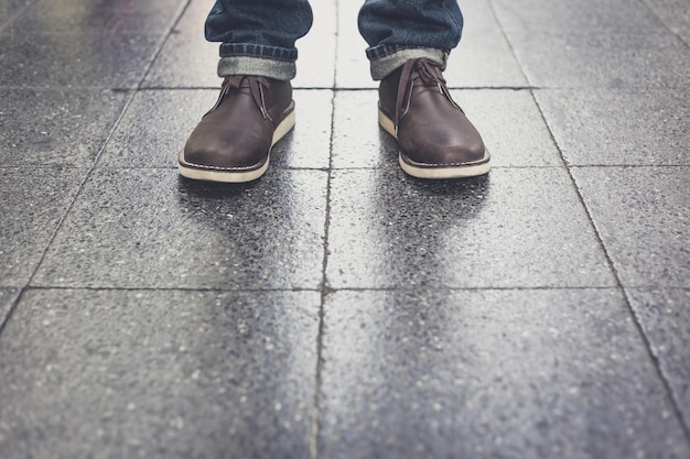 Equipaggi le blue jeans d&#39;uso e gli stivali di cuoio che stanno sul pavimento del mattone