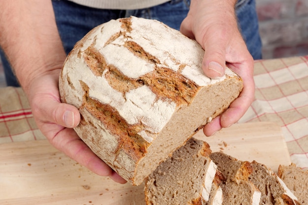 Equipaggi le mani con pane fresco sulla tavola di legno