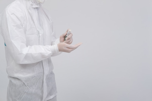 Equipaggi lo scienziato che indossa l'abbigliamento protettivo uniforme biologico, la maschera, i guanti con l'erogatore disinfettante della mano per disinfettare i batteri del virus