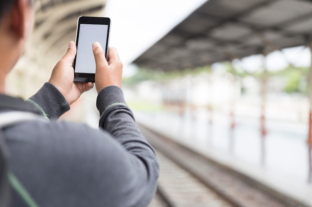 Equipaggi lo smartphone della tenuta con lo zaino alla stazione ferroviaria