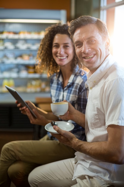 Equipaggi mangiare la tazza di tè e la donna che utilizza la compressa digitale nel supermercato