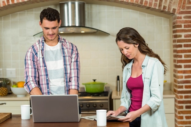 Equipaggi usando il giornale della lettura della donna e del computer portatile sul worktop della cucina