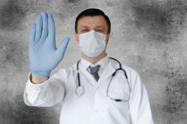 Equipaggiamento preventivo del personale medico contro il coronavirus. Medico maschio in maschera facciale che mostra il segnale di stop con la mano.
