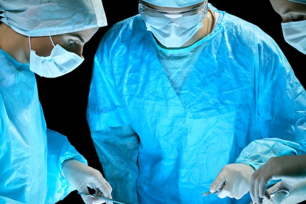 Equipe medica che esegue l'operazione. Gruppo di chirurgo al lavoro in sala operatoria nei toni del blu.