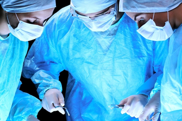 Equipe medica che esegue l'operazione. Gruppo di chirurgo al lavoro in sala operatoria nei toni del blu.