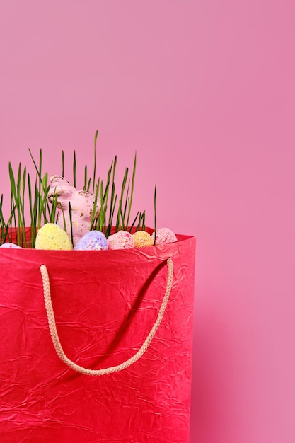 Erba succosa fresca verde e uova dipinte multicolori e coniglio in borsa della spesa rossa su sfondo rosa con spazio per la copia