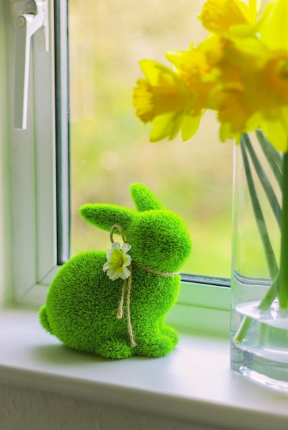 Erba verde Coniglio di Pasqua e fiori gialli in vaso sul davanzale Figurina coniglietto di primavera e narcisi