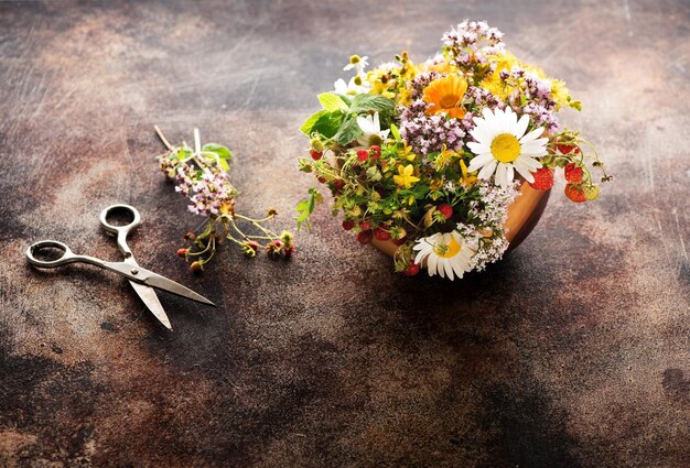 Erbe e fiori curativi in una ciotola di legno per preparare tisane e forbici su uno sfondo di cemento marrone