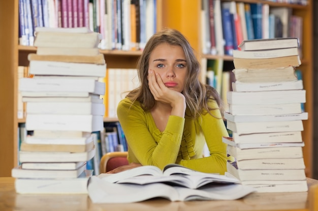 Esaurita bella studentessa studiando tra pile di libri