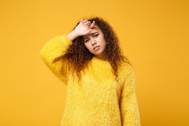 Esausta giovane ragazza afroamericana in maglione di pelliccia in posa isolata su sfondo giallo arancione ritratto in studio. Persone sincere emozioni concetto di stile di vita. Mock up spazio di copia. Mettere la mano sulla testa.