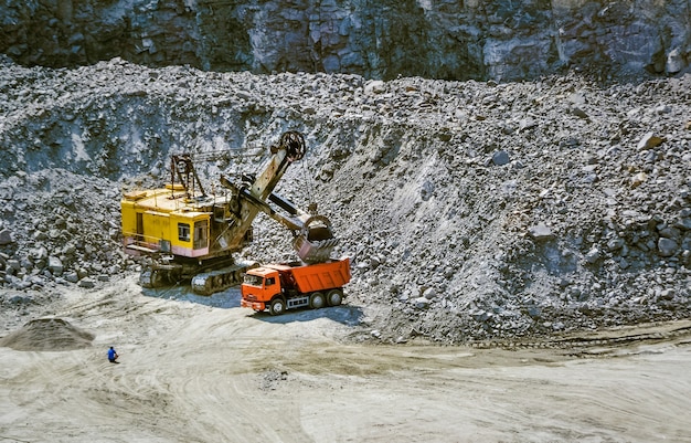 Escavatore enorme, camion e uomo in piedi accanto alla cava di granito