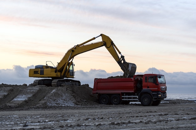 Escavatore giallo che lavora al cantiere. La costruzione della strada.