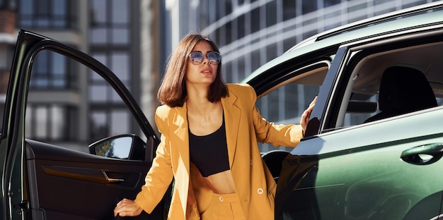 Esce dal veicolo Giovane donna alla moda in cappotto color bordeaux di giorno con la sua auto