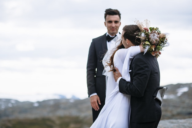 Esci dalla cerimonia in cima alla montagna, lo sposo abbraccia la sposa sullo sfondo del maestro delle cerimonie