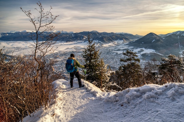 Escursionista con bastoncini da trekking e zaino guardando dalla cima della collina in inverno paesaggio innevato Hill Cebrat sopra la città Ruzomberok Slovacchia
