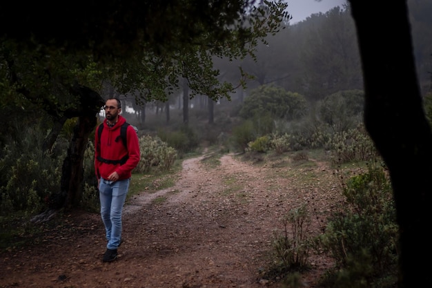 Escursionista con felpa rossa che cammina attraverso la foresta in una giornata nebbiosa