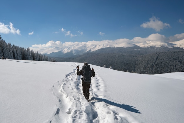 Escursionista con lo zaino che cammina sulla collina di montagna innevata in una fredda giornata invernale.