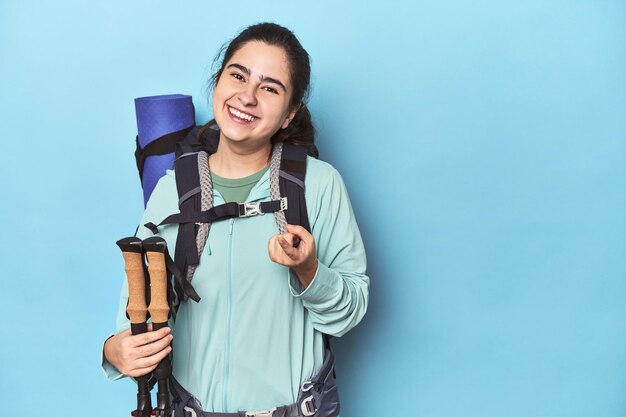 Escursionista con zaino e bastoncini sul blu che punta il dito verso di te come per invitarti ad avvicinarti