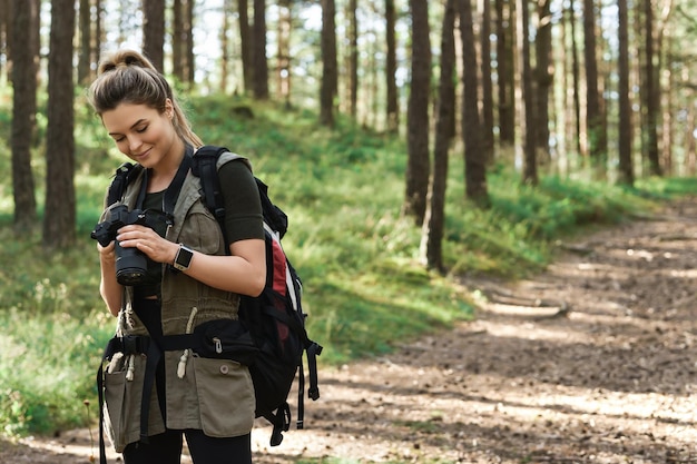 Escursionista donna che utilizza la moderna fotocamera mirrorless nella foresta verde