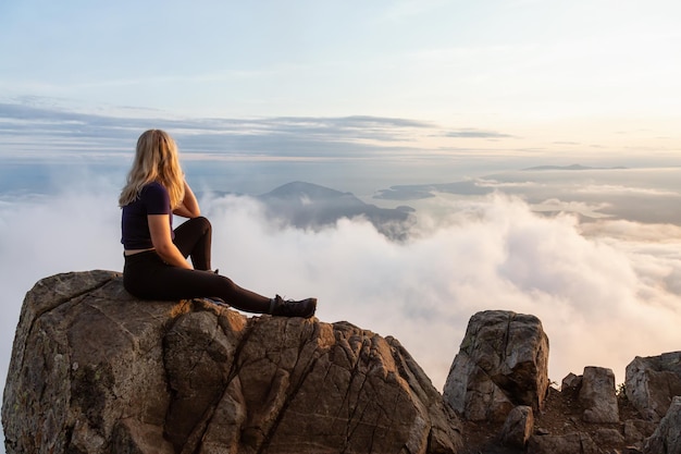 Escursionista femminile avventuroso sulla cima di una montagna coperta di nuvole durante un vibrante tramonto estivo