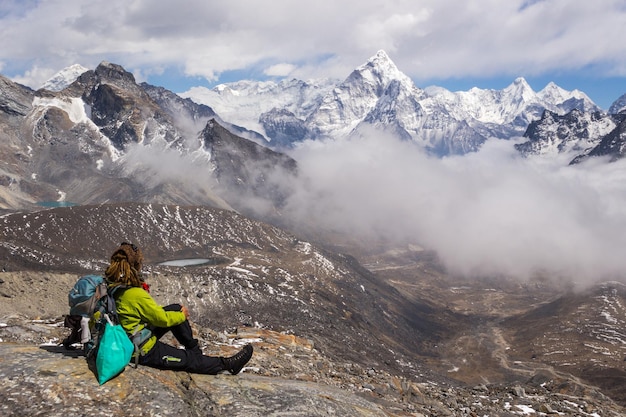 Escursionista giovane donna con zaino e bastoncini da trekking è seduto e guardando la montagna Ama Dablam. Cielo nuvoloso. Himalaya, Nepal.