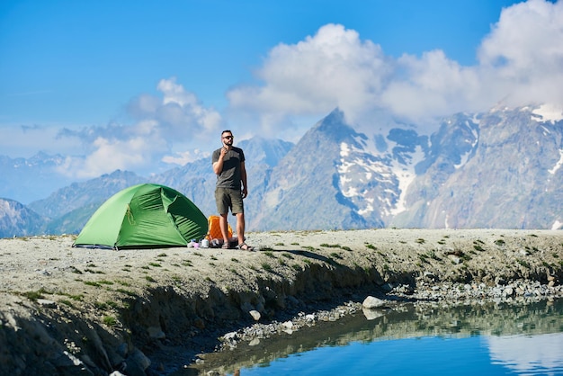 Escursionista in pantaloncini in piedi vicino alla tenda del campo in montagna