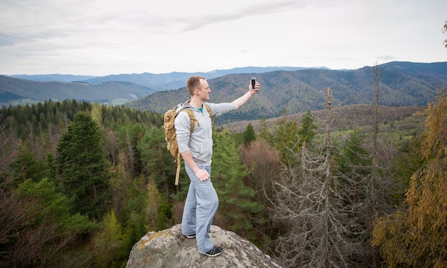 Escursionista in piedi sulla cima di una roccia e fa selfie sul suo telefono