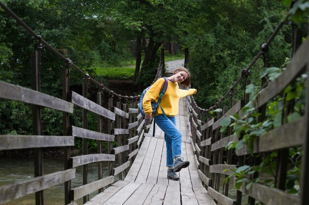 Escursionista ragazza con uno zaino in piedi sul ponte sospeso