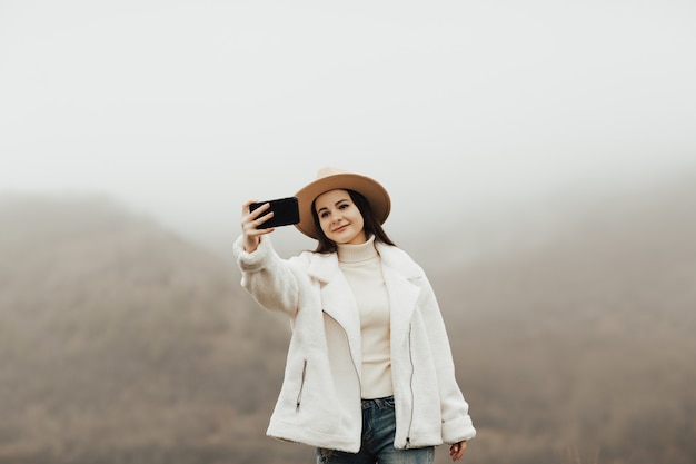 Escursionista ragazza prendendo un selfie sullo sfondo di uno splendido scenario della natura utilizzando il telefono cellulare.