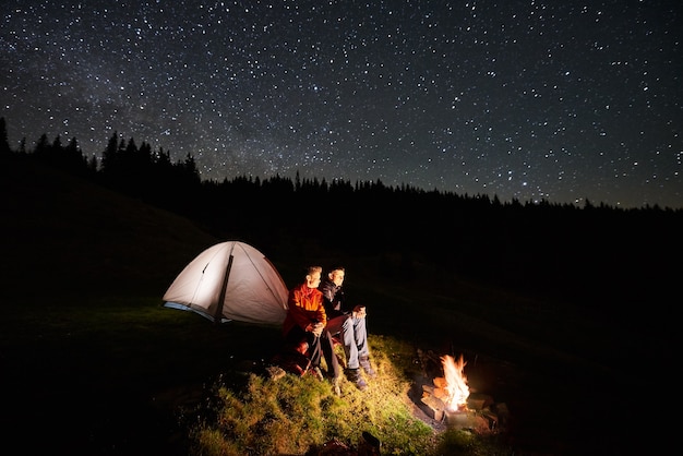 Escursionisti vicino al fuoco e tenda turistica di notte