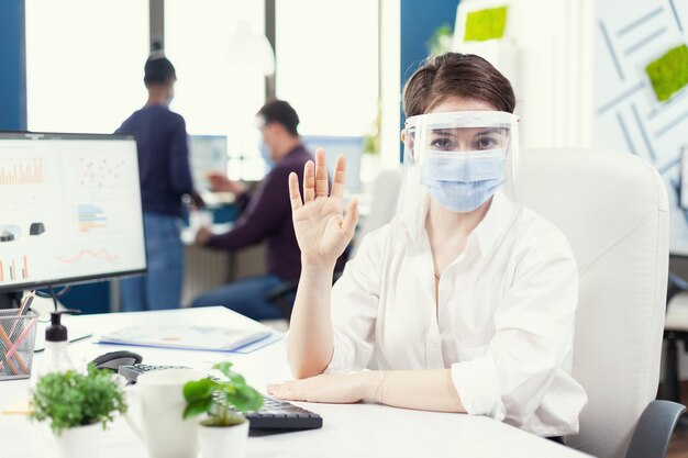 Esecutivo che indossa maschera facciale e scudo di protezione che comunica con il cliente durante covid-19..0 Pov del manager che parla con il team remoto durante la conferenza online mentre i colleghi lavorano in backgroun