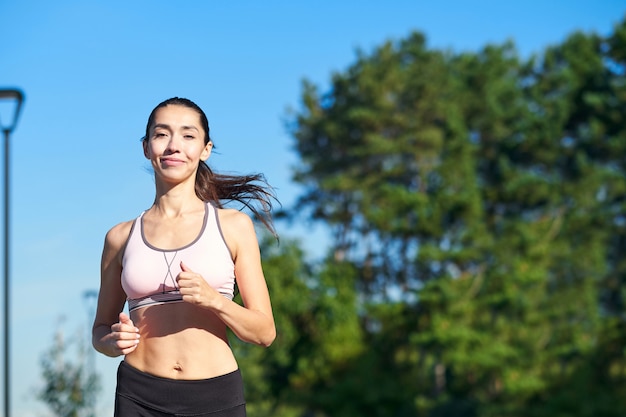 Esecuzione di donna. Corridore femminile che pareggia durante l'allenamento all'aperto in un parco. Bella ragazza in forma. Modello di fitness all'aperto. Perdita di peso