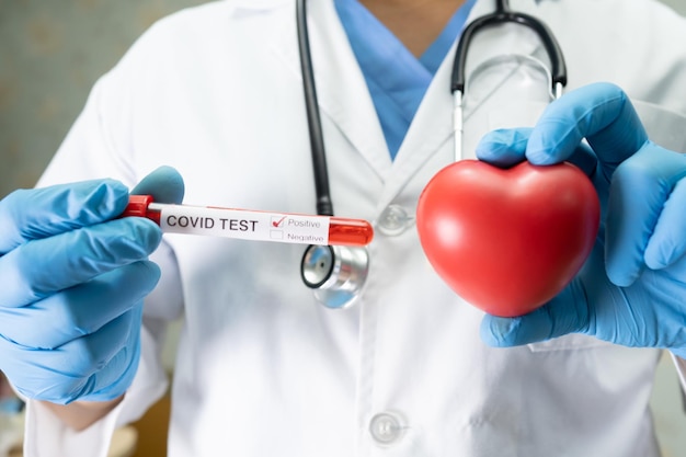 Esemplare di infezione del sangue positivo nel tubo di prova per il coronavirus COVID-19 in laboratorio Scienziato che tiene un cuore rosso per incoraggiare il paziente in ospedale