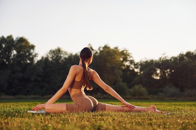 Esercizi della colonna vertebrale La giovane donna in abiti da yoga è all'aperto sul campo