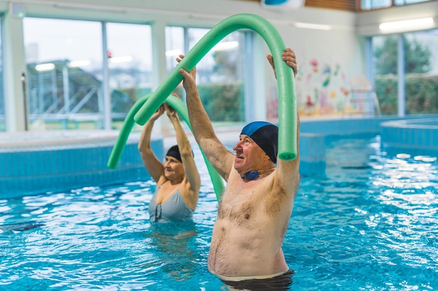 Esercizi di fitness in piscina al coperto adulti anziani caucasici che fanno esercizi di aerobica con piscina di schiuma