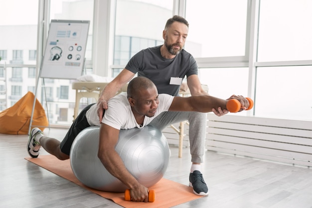 Esercizi di riabilitazione. Bello piacevole uomo che lavora sodo sdraiato sul medball mentre si allena