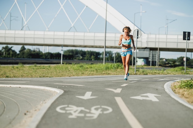 Esercizio di donna in esecuzione per adulti all'aperto. Corre sul lungomare della città e ascolta musica.