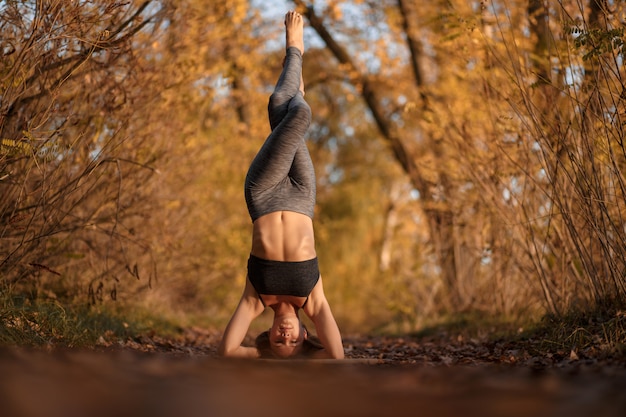 Esercizio di pratica di yoga della giovane donna al parco di autunno con le foglie gialle. Stile di vita sportivo e ricreativo