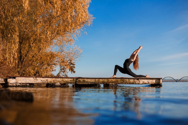 Esercizio di yoga di pratica della giovane donna al pilastro di legno calmo con la città. Sport e tempo libero in città