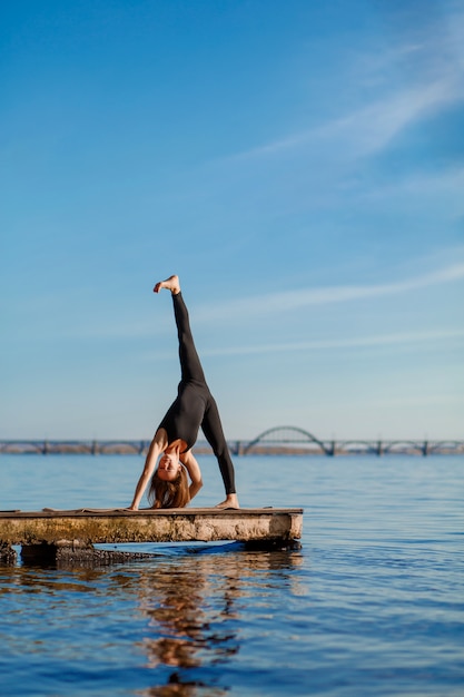 Esercizio di yoga di pratica della giovane donna al pilastro di legno calmo con la città